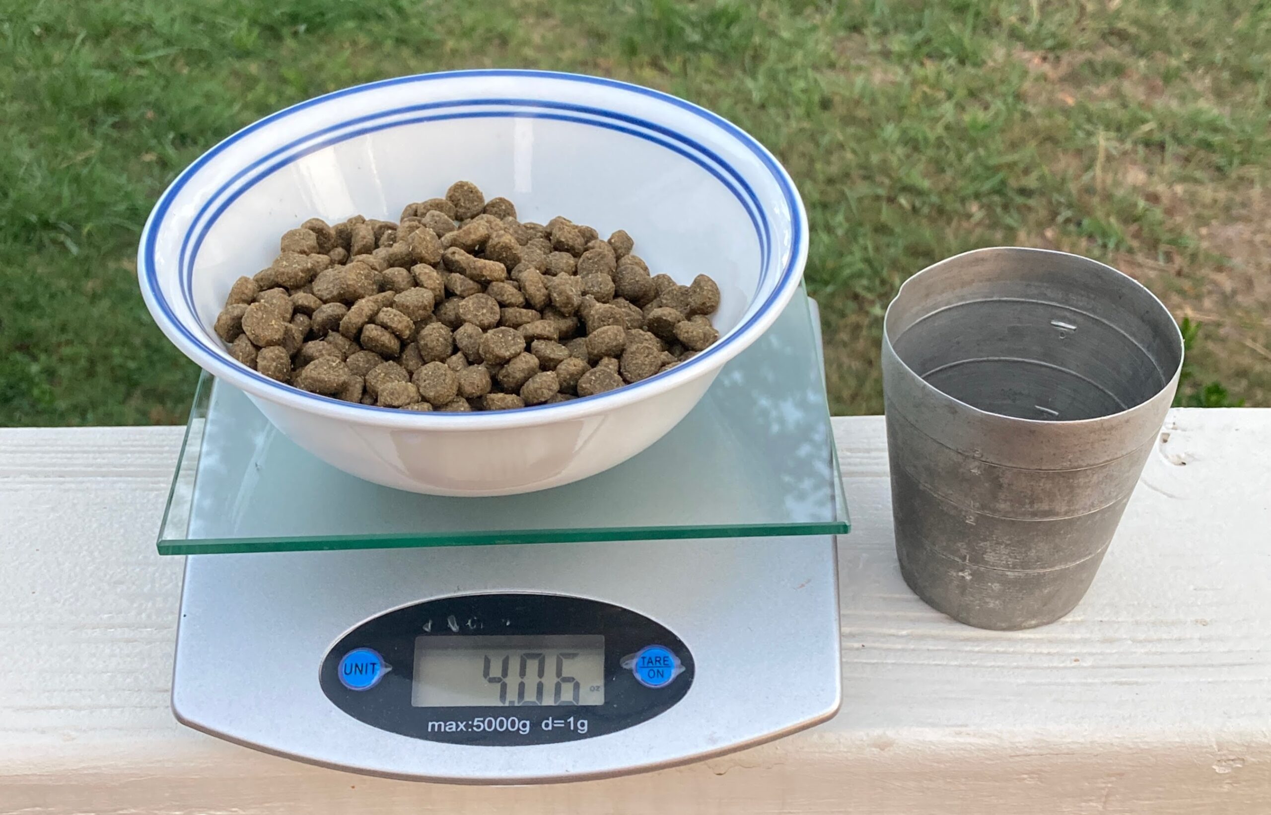 A hand holding a measuring cup of dry puppy kibble over a kitchen counter next to a puppy bowl